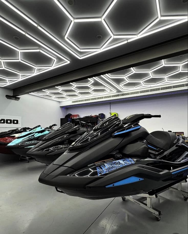Black jet skis parked in a modern garage with striking hexagonal LED ceiling lights.